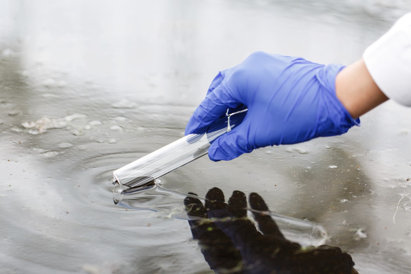 gloved hand taking contaminated water sample from water source